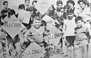 Black and white photograph of children holding kites which say Allende