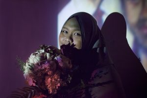 Photograph of girl holding flowers by artist Charmaine Poh. Aini holds flowers as she looks into the camera.