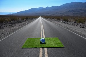 Photograph of a foil ball on a square of grass placed on a long road which disappears into landscape by artist Kyle Giacomo, resident artist at GlogauAIR 2019