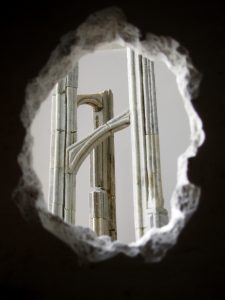 Photograph taken through a hole in a wall looking into the room at a stone architectural model. By artist Marcos Kaiser, resident at GlogauAIR January 2020